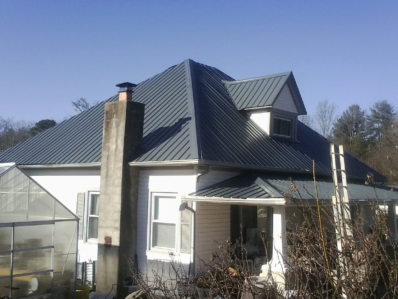 Dark blue standing seam metal roof on a white farmhouse with dormer — Slate & Tile Roof Repair by Roofing Brothers in Wana
