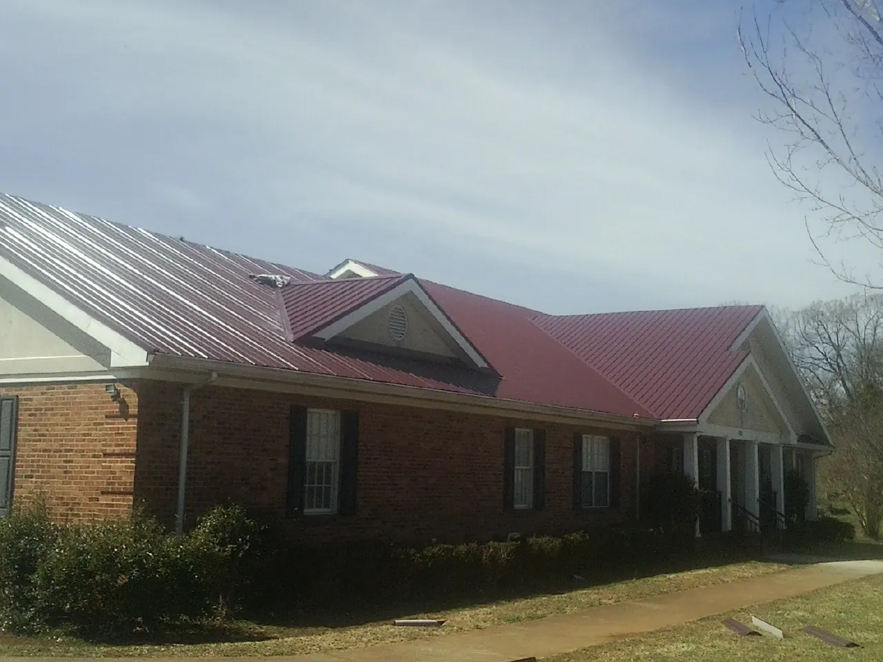 Red metal roof with gabled entries on a long brick building, from a Hail Damage Roof Repair job in Wana