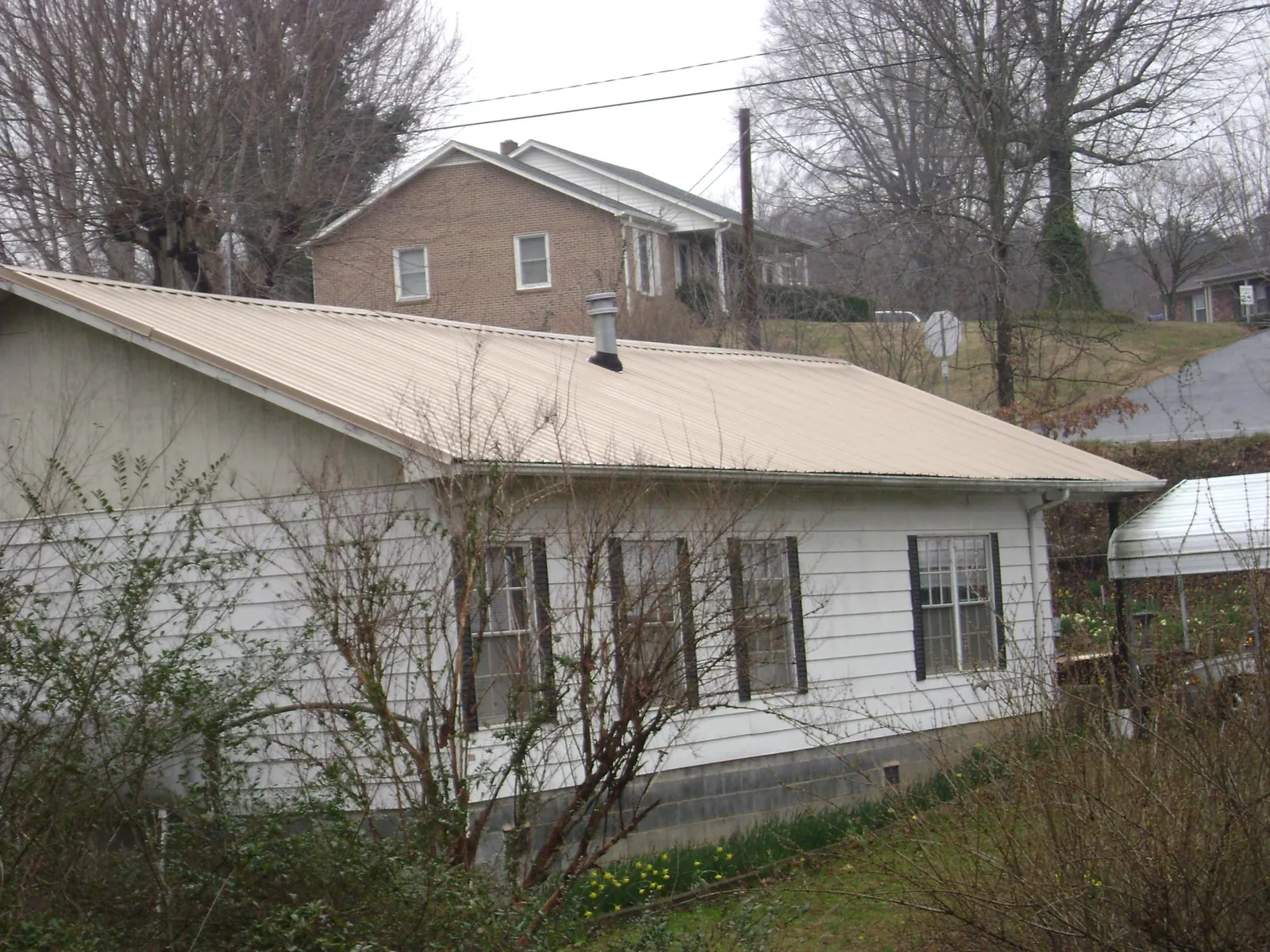 Tan metal roof on a white sided house set into a hillside — Commercial Roofing by Roofing Brothers in Wana